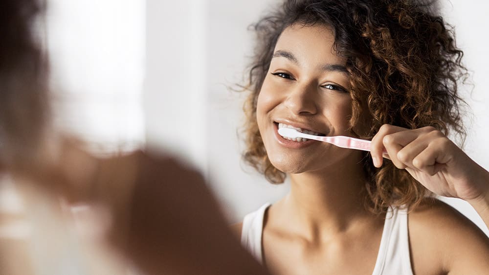 Jeune fille se brosse les dents avec le sourire devant un miroir.