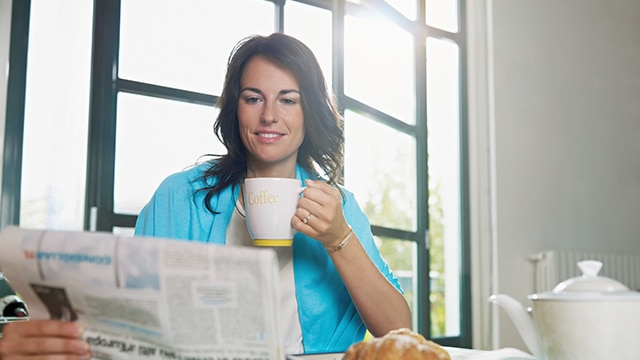 Une fille buvant un café et regardant le journal