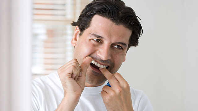 Un homme se nettoyant les dents avec du fil dentaire